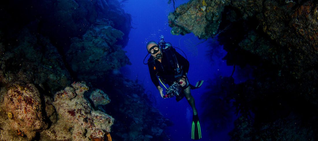 A scuba diver exploring the ocean near a cave, surrounded by vibrant marine life and the beauty of underwater scenery.