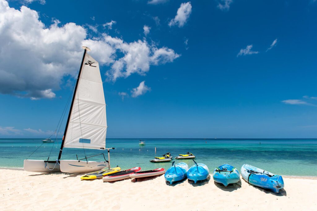 A row of kayaks, sailboat, and kayaks on the beach