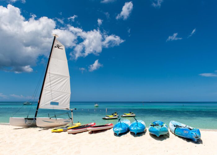 A row of kayaks, sailboat, and kayaks on the beach